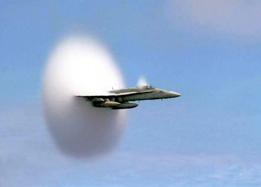 F18 Jet flys by a carrier and water precipitates from the shock wave in a donut-shaped cloud